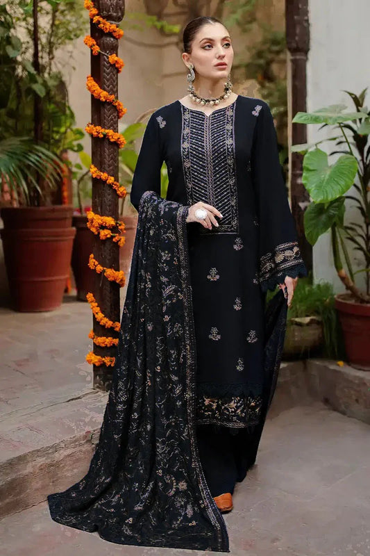 Woman in black embroidered outfit with dupatta standing outdoors.