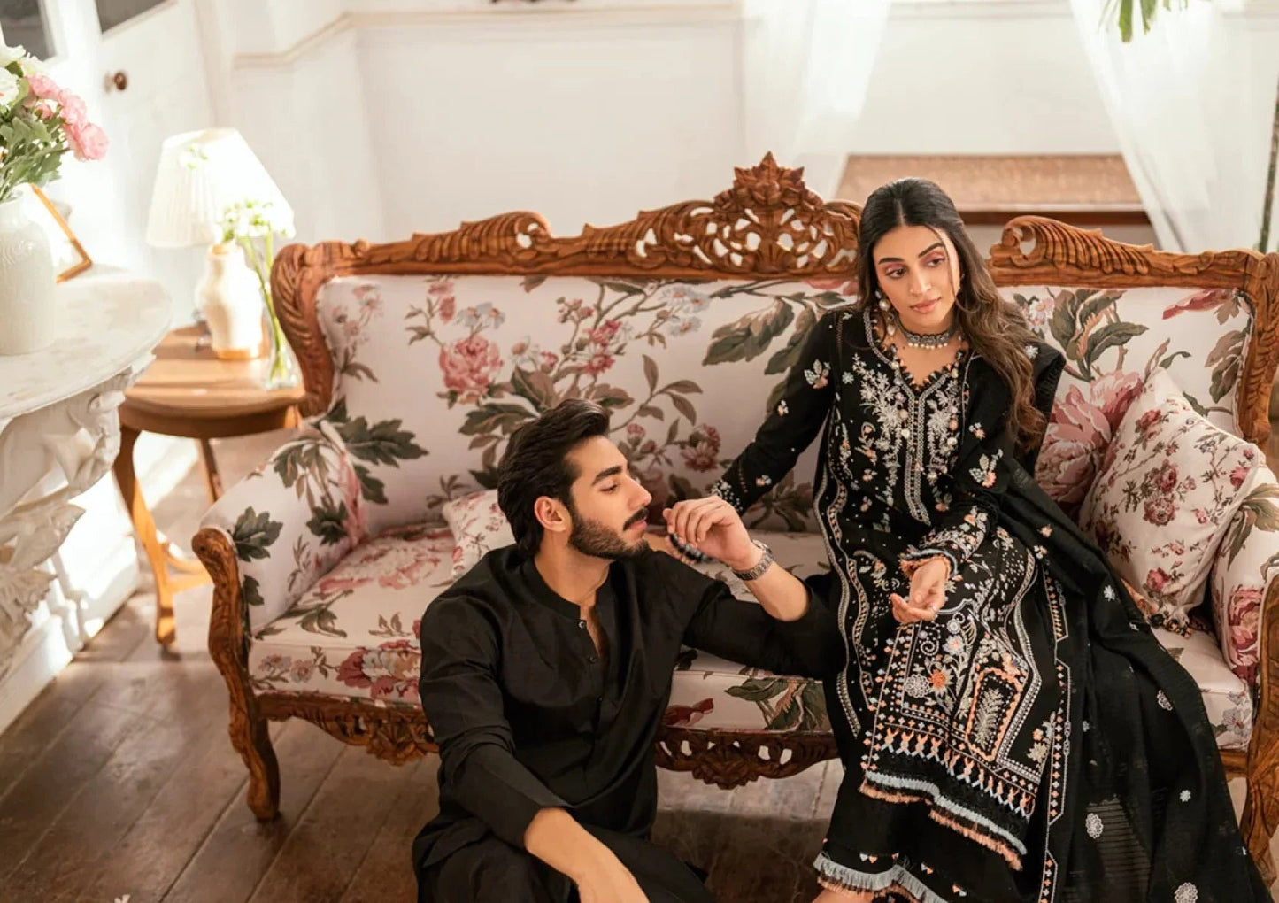 Two women sitting on a decorative chair with floral patterns.