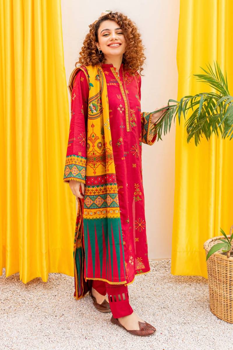 Woman in a colorful traditional outfit standing in front of yellow curtains.