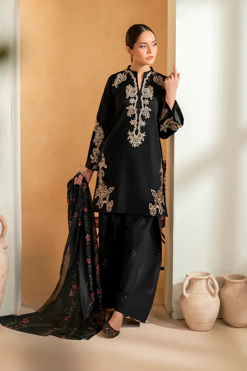 Woman in a black embroidered outfit standing against a beige wall with decorative vases.