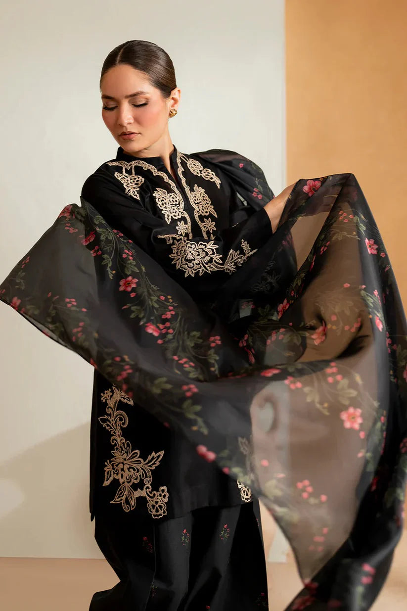 Woman wearing a black outfit with floral and embroidery details, holding a matching black scarf.