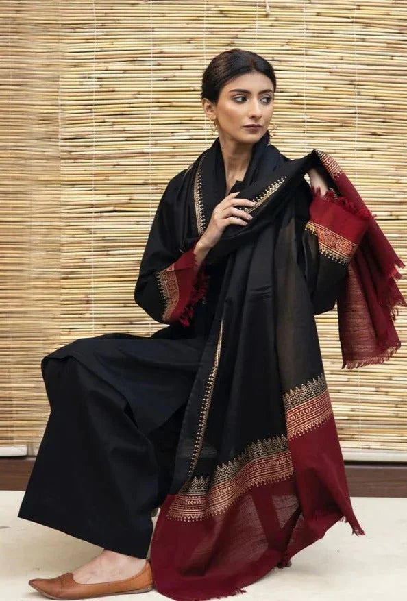 Woman wearing a black and red saree with a bamboo wall background