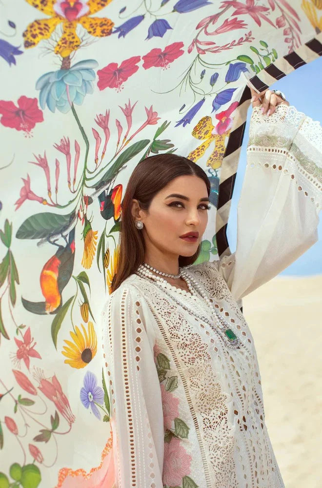 Woman in a white embroidered outfit holding a colorful floral parasol against a desert background