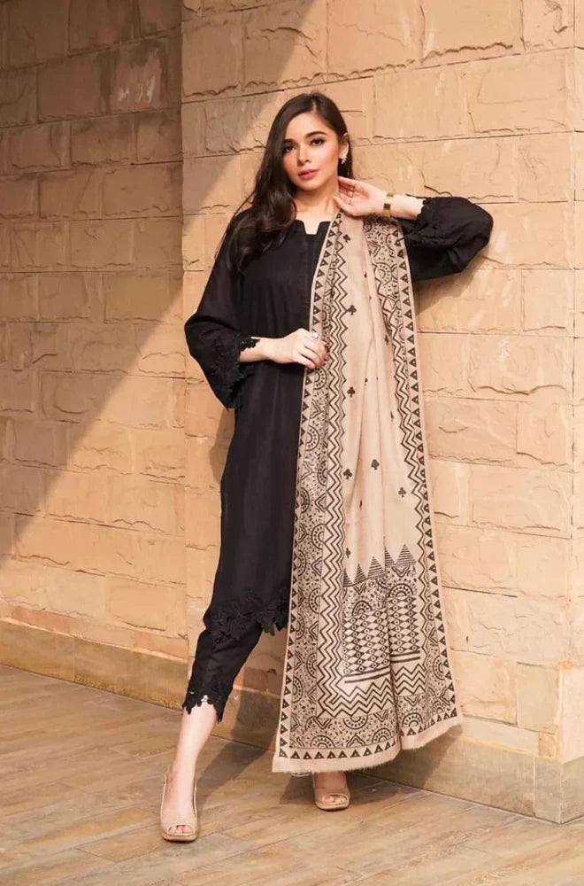 Woman wearing a black outfit with a beige embroidered scarf against a stone wall.