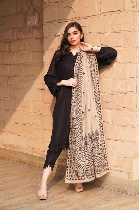 Woman wearing a black outfit with a beige embroidered scarf against a stone wall.