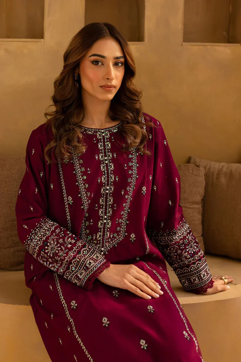 Woman wearing a maroon embroidered traditional outfit sitting on a beige couch.
