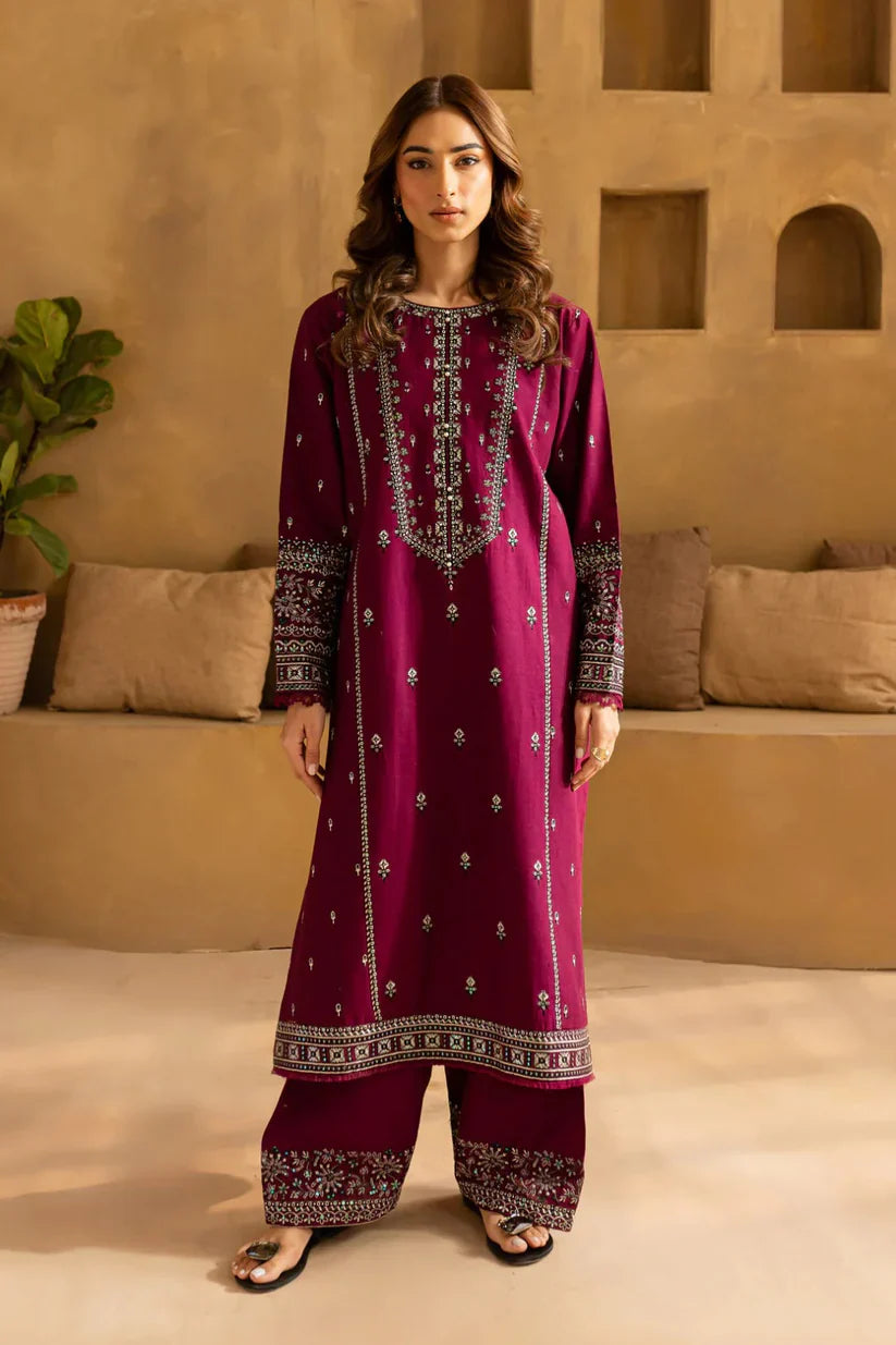 Woman wearing a magenta embroidered traditional outfit in a beige room.