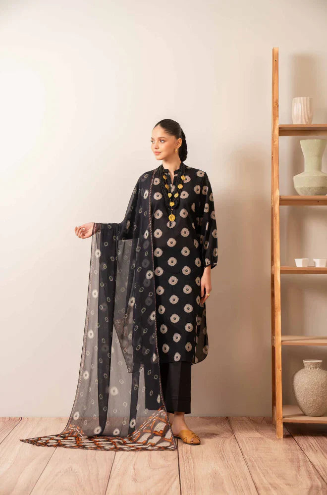 Woman wearing a black floral outfit with a sheer dupatta in a minimalistic room.