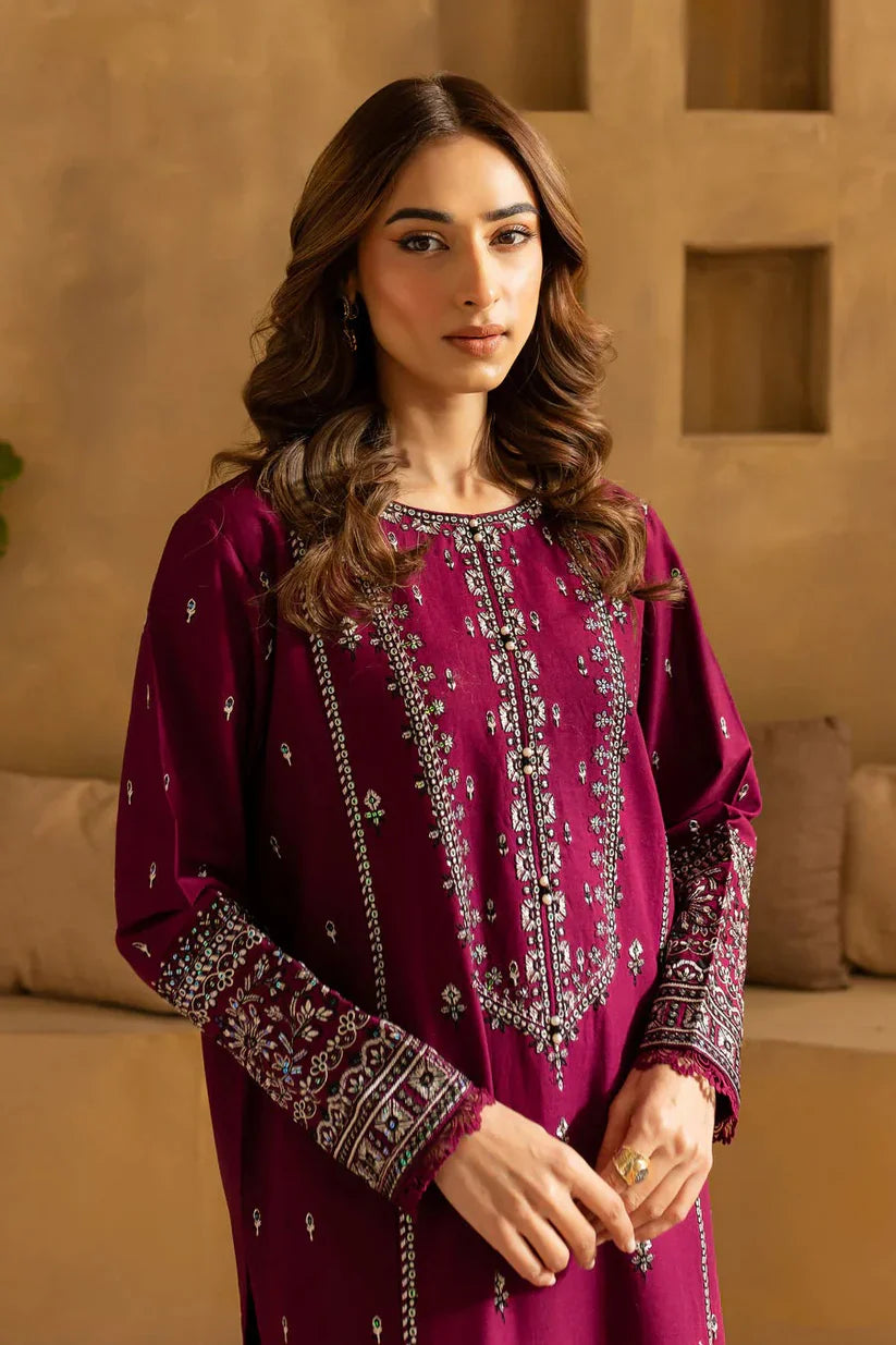 Woman wearing a magenta embroidered traditional outfit against a beige wall.