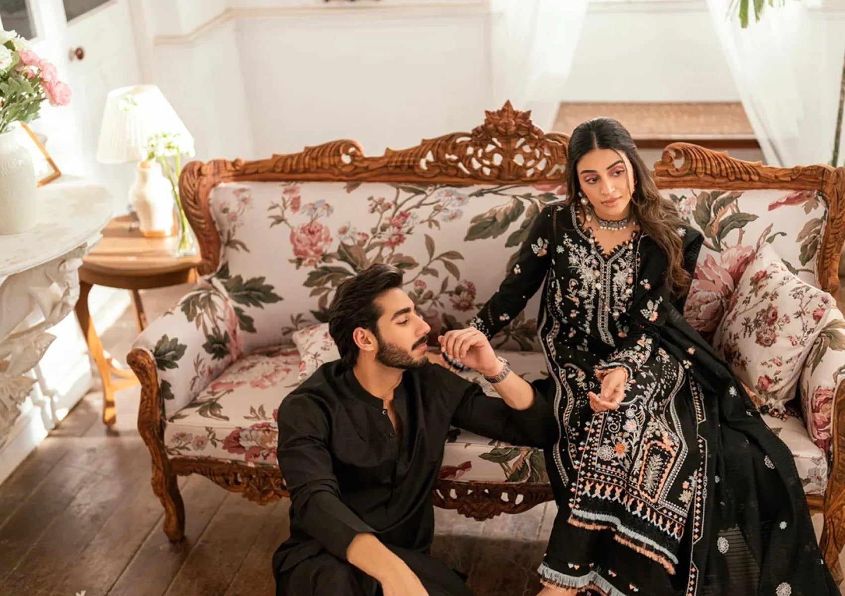 Two women sitting on a decorative chair with floral patterns.